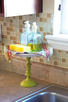 soap and lotion bottles are sitting on a tray in the kitchen sink next to a window