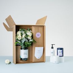 an open box with some flowers in it next to a bottle of lotion and soap