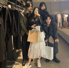 three people taking a selfie while holding shopping bags in a clothing store with clothes on racks behind them