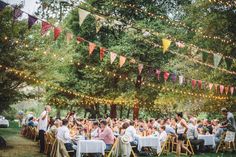 a group of people sitting at tables in the middle of a park with bunting