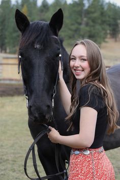 a girl is standing next to a black horse and smiling at the camera while holding it's bridle