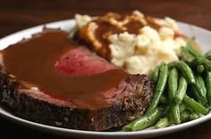 a steak dinner with mashed potatoes, green beans and gravy on a white plate