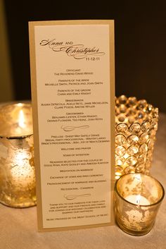 a menu card sitting on top of a table next to two lit votives