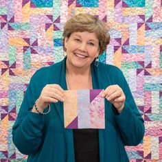 a woman holding up a piece of paper in front of a quilt