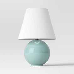 a light blue lamp with a white shade on the top and bottom, sitting in front of a gray background