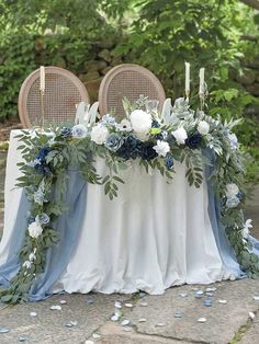 the table is set with blue and white flowers, greenery and candles on it