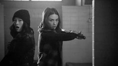 two women standing in a bathroom with one pointing at the camera while the other looks surprised