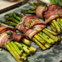 asparagus wrapped in bacon on top of a metal tray with other food items