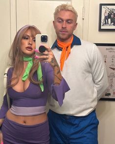 a man taking a selfie with a woman dressed in purple and green holding a cell phone