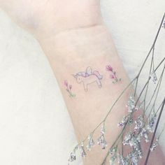 a small tattoo on the wrist of a girl with flowers and an unicorn in it