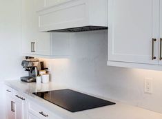 a kitchen with white cabinets and black stove top on the countertop is lit by recessed lighting