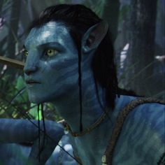 a woman with blue paint on her face holding a stick in the woods while staring at something