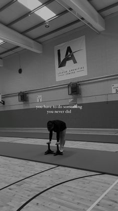 a man kneeling down on top of a basketball court next to a wall with a quote above it