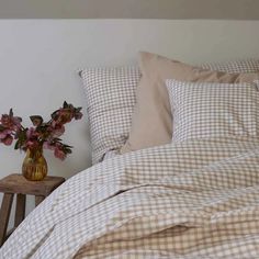 a vase with flowers sitting on top of a wooden table next to a bed covered in plaid sheets