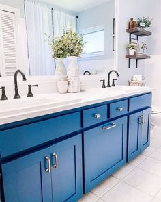 a bathroom with blue cabinetry and white counter tops, along with a vase filled with flowers