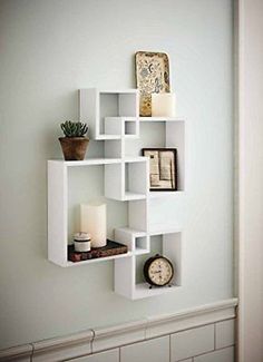 a white shelf with some books and candles on it next to a wall mounted clock