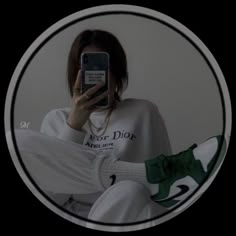 a woman taking a selfie with her cell phone in front of her face while wearing white sweatpants and green sneakers