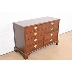 a wooden dresser with four drawers and gold leaf knobs on the top, against a white brick wall