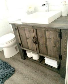 a white toilet sitting next to a wooden cabinet in a bathroom under a sink with two faucets