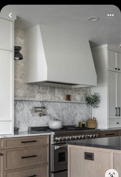 a kitchen with white cabinets and marble counter tops, an oven hood over the stove