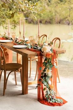 an orange table runner with flowers and candles on it is ready for the guests to sit down