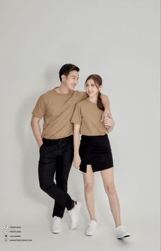 two people standing next to each other in front of a white wall wearing brown shirts and black shorts