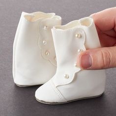 a hand is holding a small white boot with pearls on it's side and the shoe has been made out of plastic