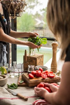 a man and woman preparing food on a kitchen counter with tomatoes, lettuce and other vegetables