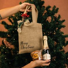 a person holding a bottle of wine next to a bag with a christmas message on it