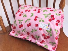 a pink pillow with cherries on it sitting on a wooden chair next to a white wall