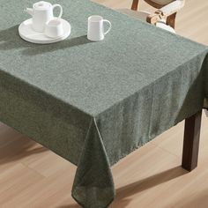 a green table cloth with two cups and saucers on it sitting on a wooden floor