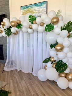 white and gold balloons are hanging from the ceiling in front of a fireplace with greenery