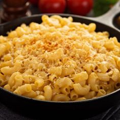 a pan filled with macaroni and cheese on top of a table next to tomatoes