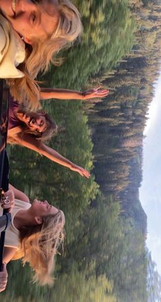 two women standing next to each other with trees in the background and water reflecting them