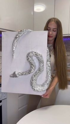 a woman holding up a piece of paper with the letter s on it in silver foil