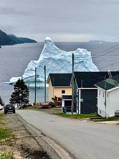 an iceberg floating in the ocean next to some houses and cars on a road