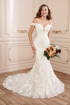 a woman in a white wedding dress holding a bouquet and posing for the camera with her hands on her hips