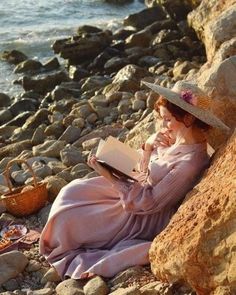 a woman sitting on the beach reading a book and holding a basket in her hand