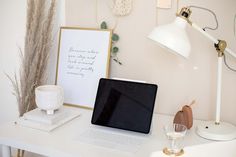 a laptop computer sitting on top of a white desk next to a lamp and vase