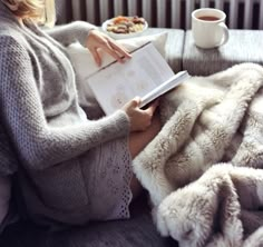 a woman is reading a book while sitting on a couch with a cup of coffee