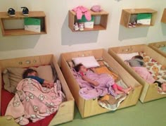 three small children sleeping in wooden boxes on the floor