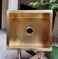 a square metal sink sitting on top of a wooden stand next to a potted plant