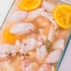 chicken and oranges are being cooked in a glass dish with water on the side