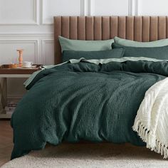 a bed with green comforter and pillows in a white room next to a brown headboard