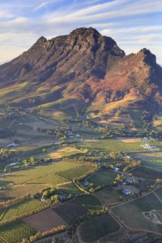 an aerial view of a mountain range with fields and trees in the foreground, surrounded by mountains