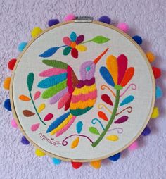 a colorful embroidered bird on a white background with pom - poms around it