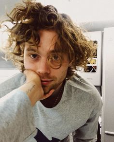 a young man with curly hair sitting in front of a refrigerator freezer looking at the camera