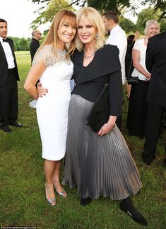 two women standing next to each other in front of people at an outdoor event on the grass