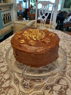 a chocolate cake with walnuts on top is sitting on a glass platter in front of a dining room table