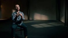 a man sitting on top of a chair in the middle of a dark room with his hands crossed